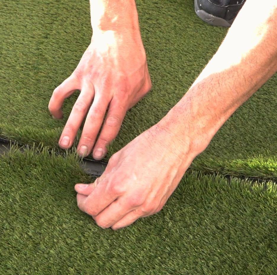 Primer plano de dos manos uniendo dos rollos de césped artificial durante una instalación